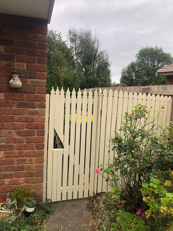 Cream picket gate and fence beside a brick house and garden