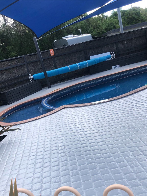 After: pool surround coated in light grey, beside the pool under a shade sail