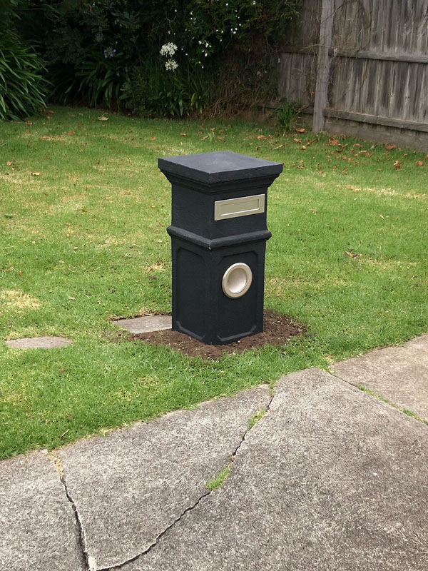 Dark grey pillar letterbox on a front lawn beside a concrete path