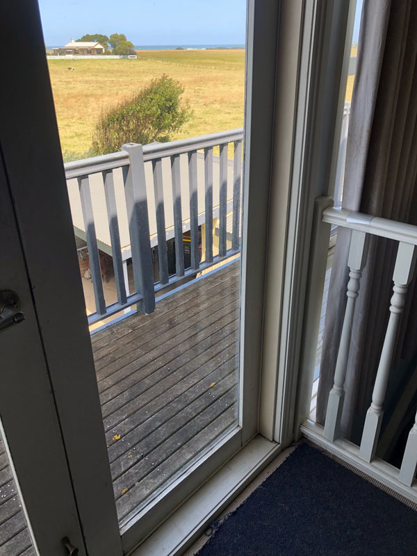 Open glass door to a balcony with a white balustrade overlooking paddocks