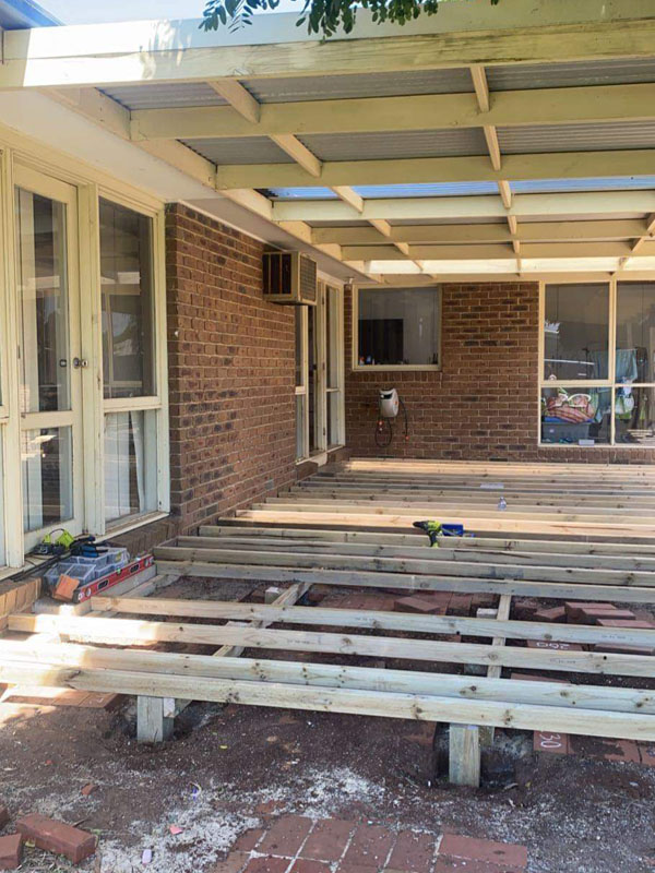 Before: timber deck frame of joists and bearers under a pergola beside a brick house