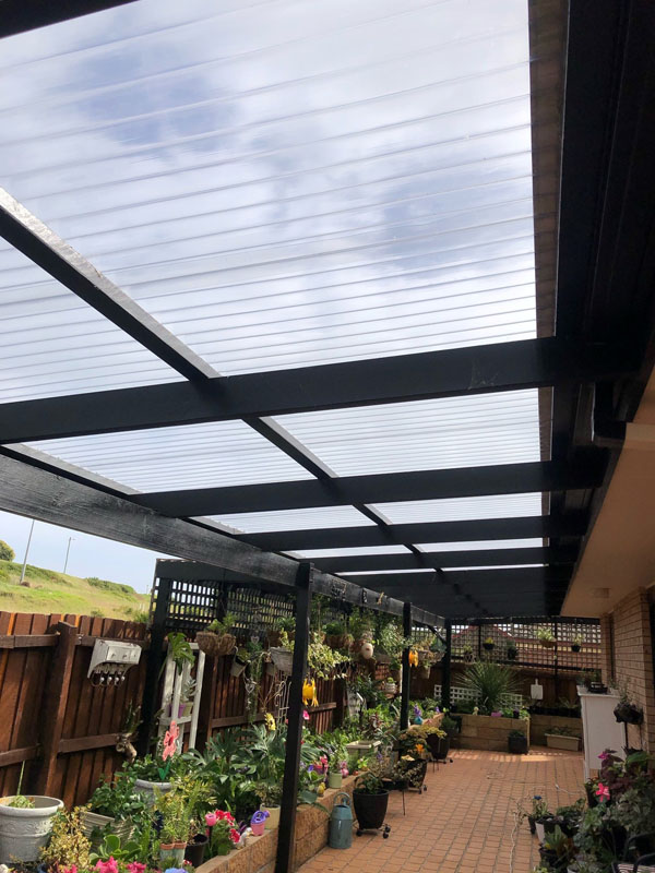 Pergola with clear roofing over a paved courtyard lined with pot plants