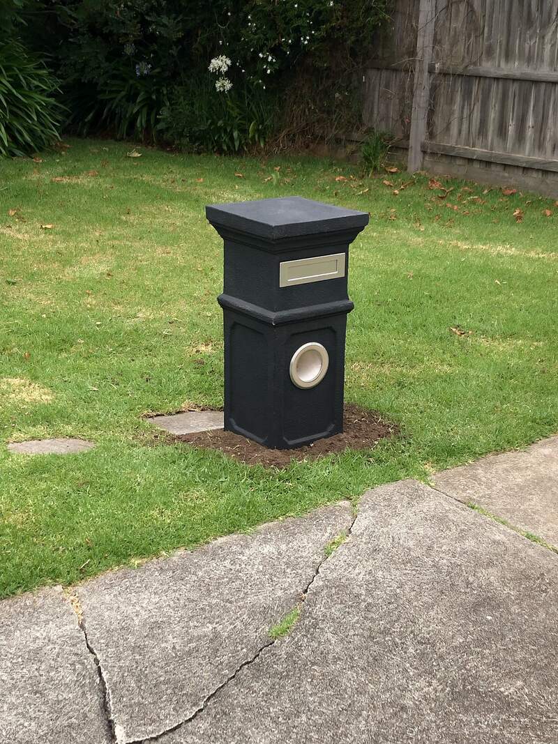 Dark grey pillar letterbox on a front lawn beside a concrete path