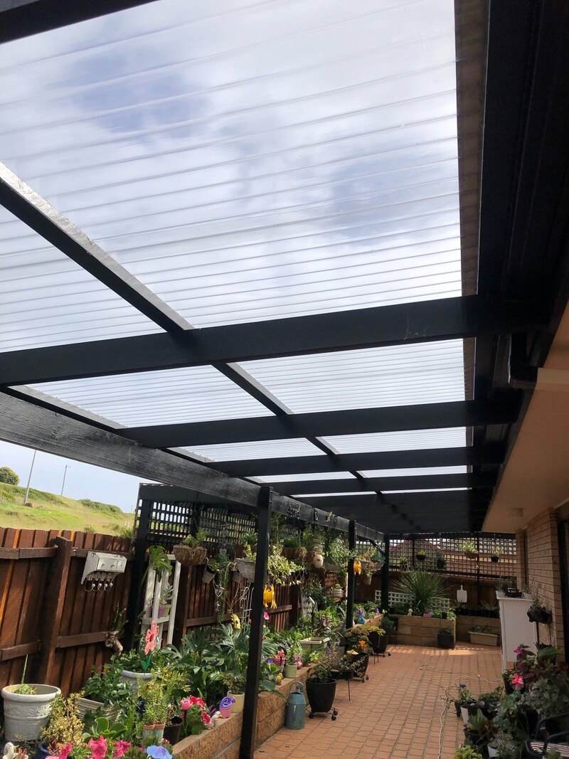 Pergola with clear roofing over a paved courtyard lined with pot plants