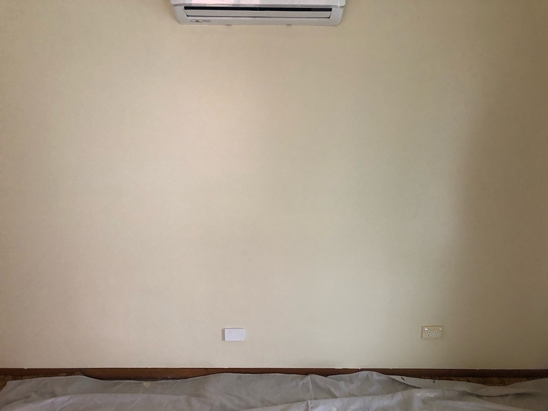 Freshly painted cream wall below a split-system air conditioner, with a drop sheet on the floor