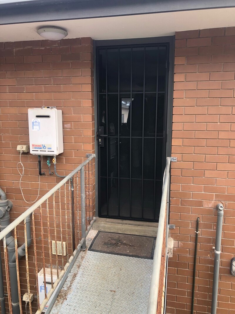 Ramp with steel handrails leading to a black security door at a brick unit