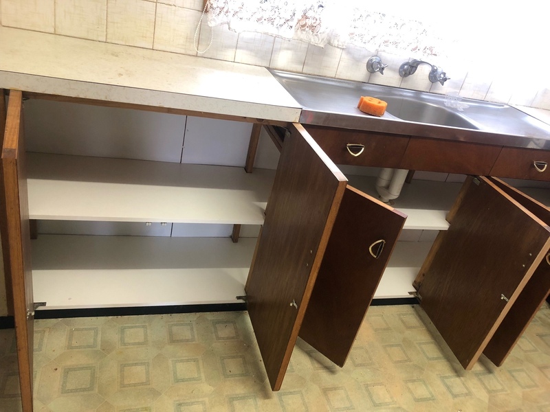 Row of timber kitchen cupboards open under a stainless steel sink, showing white shelves